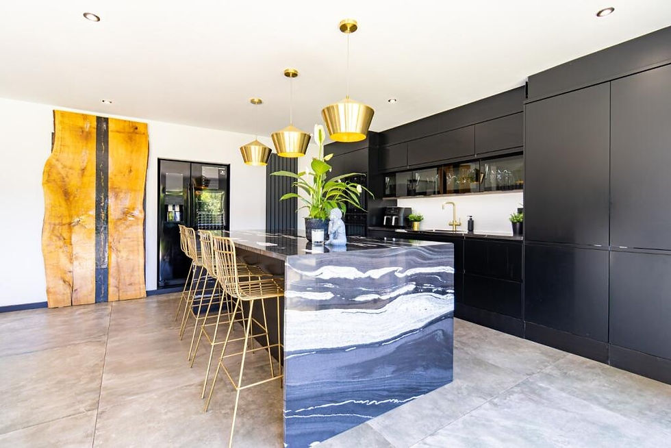 Modern kitchen with black cabinets, a marble island, gold pendant lights, and bar stools. Large wooden art piece on white wall. Bright and sleek.