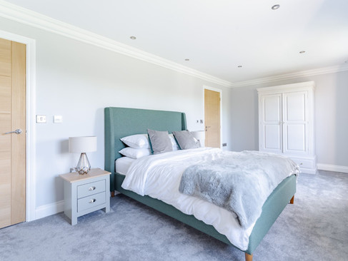 Spacious bedroom with teal upholstered bed, grey carpet, light wood doors, white wardrobe and matching bedside tables.