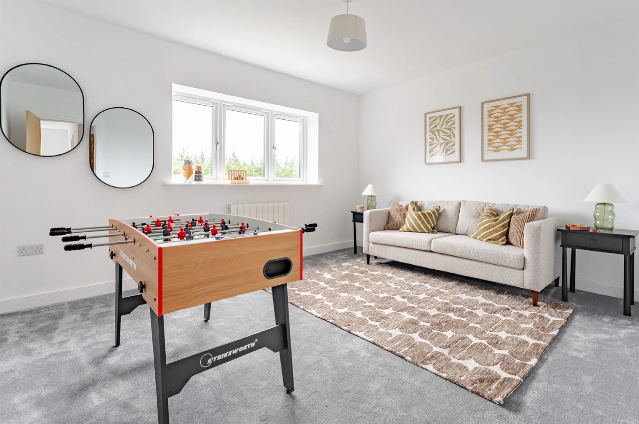 Modern living room with a foosball table, round mirrors, and a beige sofa. Bright window light, abstract art, and cozy atmosphere with a patterned rug.