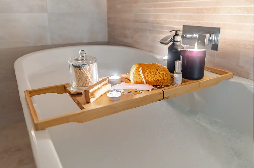 Bath tray over tub with a candle, brush, sponge, and toiletries. Warm beige tiles in background create a relaxing ambiance.
