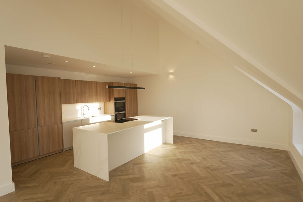 Modern kitchen with white island, wood cabinets, and built-in oven. Herringbone wood floor, minimal decor, warm lighting, spacious feel.
