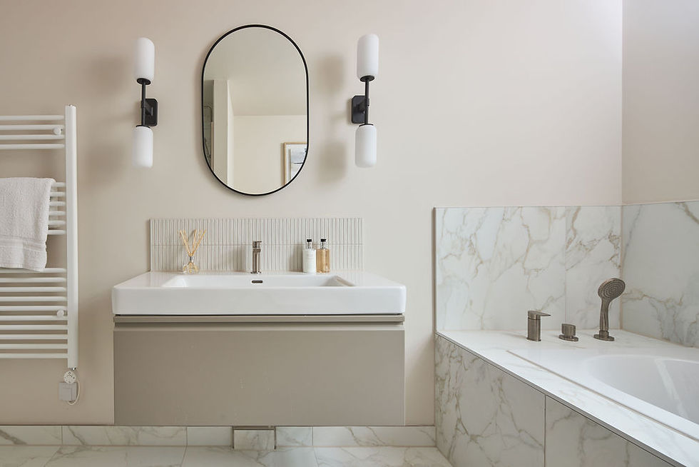 Modern bathroom with white marble tiles, oval mirror, dual sconces, a sink with soap dispensers, and a towel on a heated rack.
