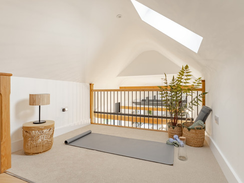 Bright mezzanine landing with skylight, wooden balustrade, yoga mat and woven side table overlooking the open-plan space below.