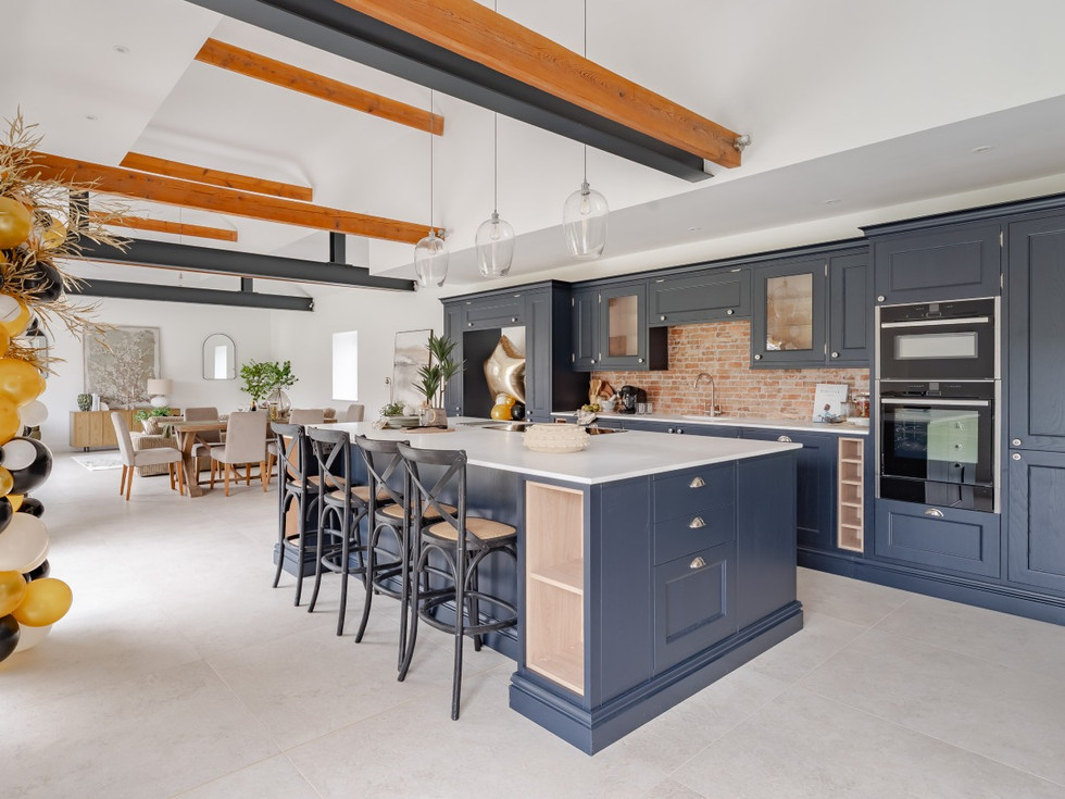 Spacious open-plan kitchen with navy shaker cabinetry, large island with bar stools, brick splashback and exposed timber beams overhead.
