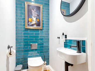 Compact cloakroom with turquoise subway tiles, wall-hung toilet, small basin and framed artwork above.