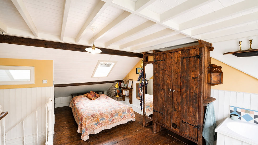 Cozy attic bedroom with a bed, rustic wooden wardrobe, white beamed ceiling, and colorful decor; no people.