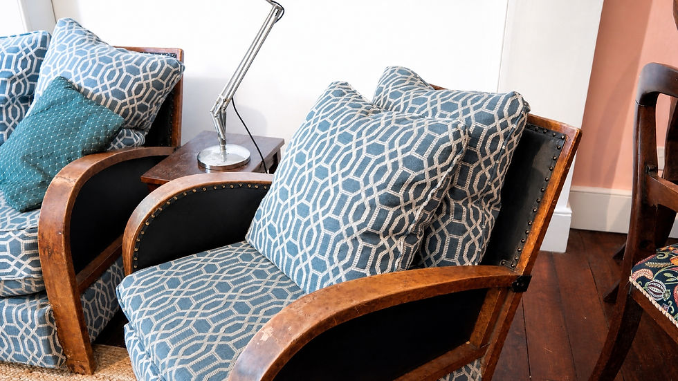 Blue patterned armchairs with matching pillows beside a small lamp table on a wood floor in a cozy sitting room.