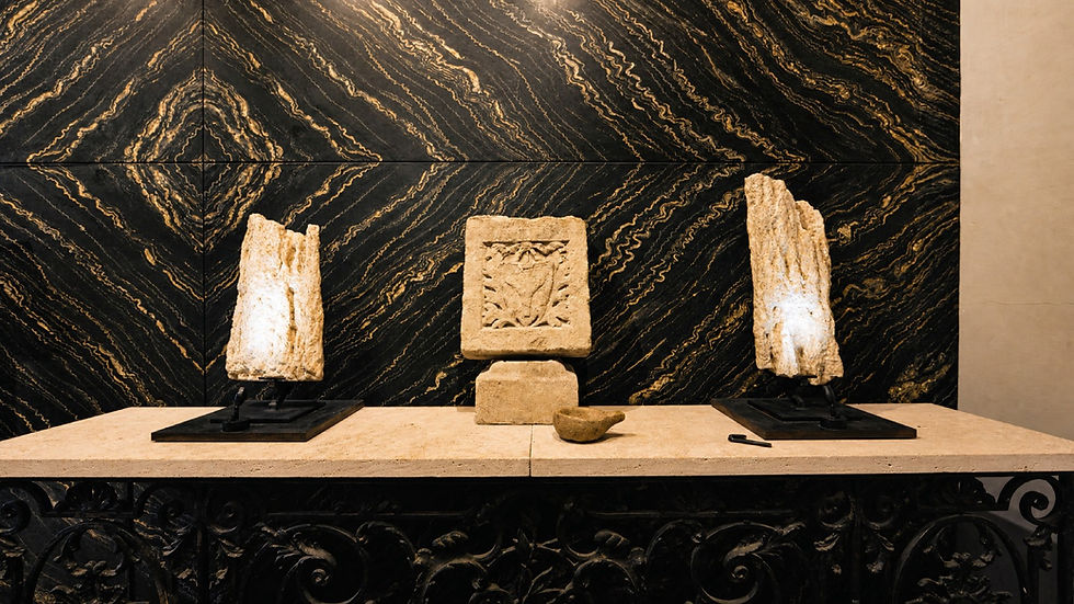 Stone artifacts displayed on a beige table before a black-and-gold marbled wall, with ornate metalwork below.