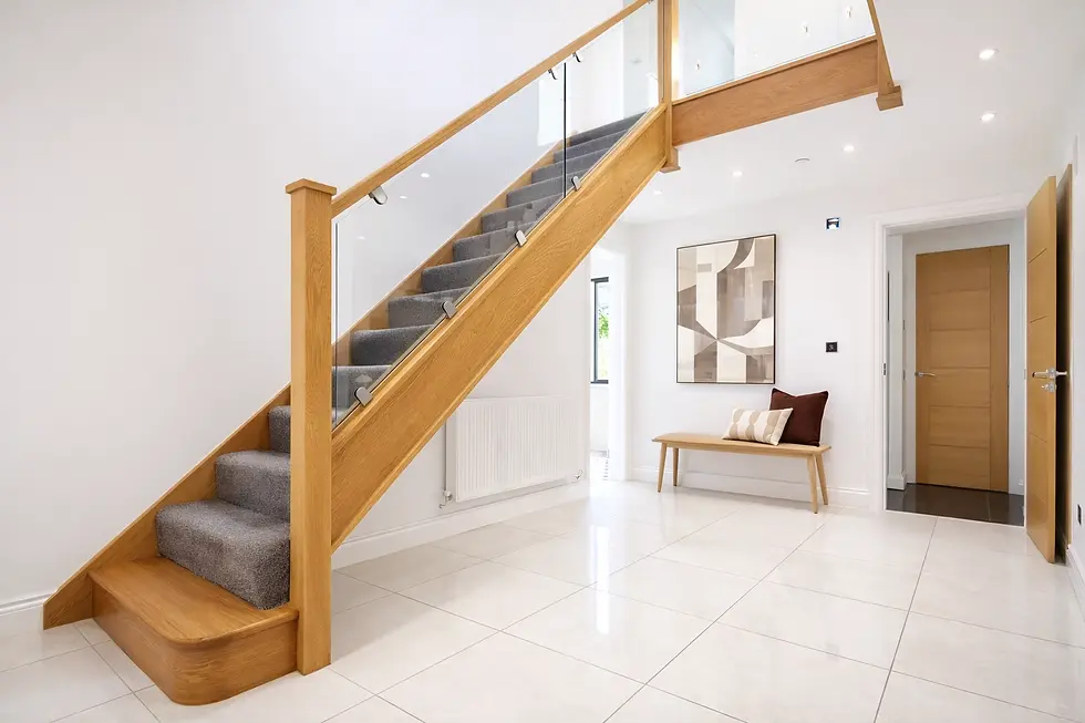 Wooden staircase with glass railing in modern hallway. Artwork and bench with cushions on white tiled floor, doors on either side.