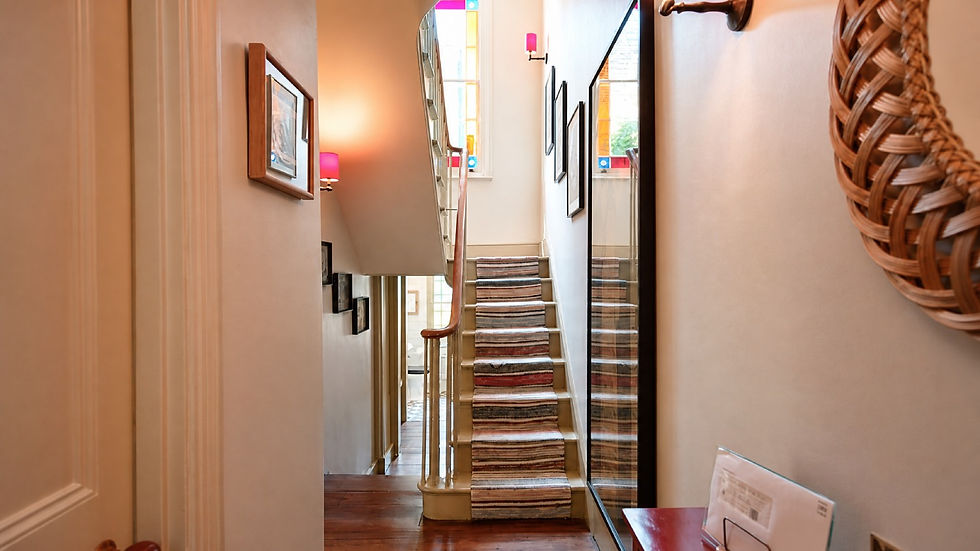 Narrow hallway with striped carpeted stairs, framed art, pink wall sconces, and stained-glass windows in a warm home interior.