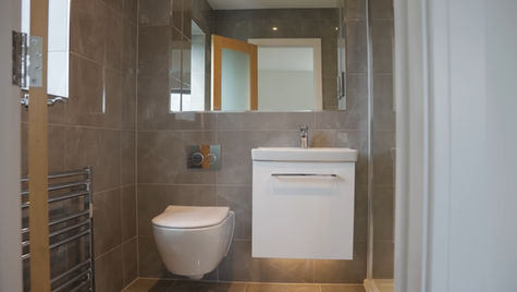 Modern bathroom with gray tiled walls, featuring a wall-mounted toilet, white sink with mirror, and a glass shower enclosure. Clean and minimalistic design.