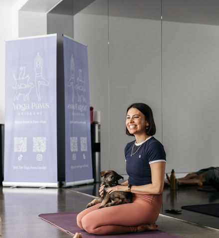 Woman sitting on yoga mat with puppy near a Yoga Paws banner in studio