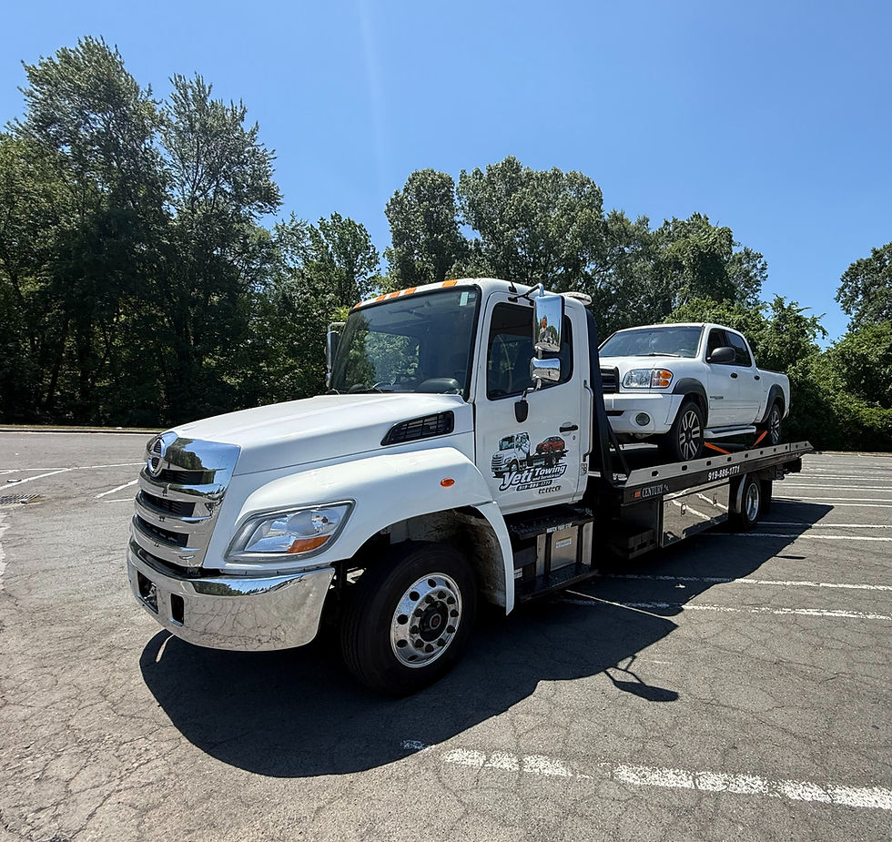 White tow truck towing a white truck in a parking lot. Logo displayed with Yeti Towing and Service LLC. Trees behind.