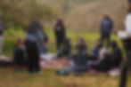 A group of gastronomes enjoying food in an open sac sitting on the ground in a picnic setup