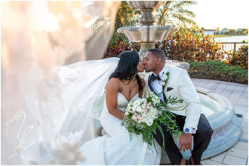 Bradenton Wedding Photographer, The bride's veil blows towards the camera as she and groom share a kiss while sitting on the fountain at the Mirabay Club