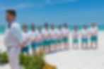 Sarasota Wedding Photographer groomsmen wearing teal shorts don sunglasses as they watch the tropical wedding ceremony