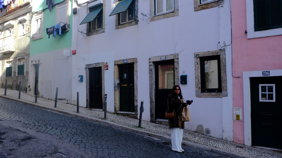 Woman standing on a sloped street lined with pastel colored houses and shuttered windows in Lisbon Portugal