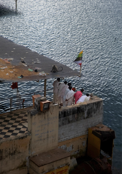 Group of men standing by a riverside platform near water with a monkey nearby in Pushkar Rajasthan India, capturing a candid moment of daily life