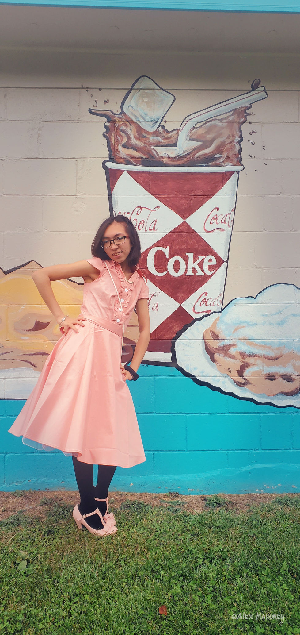Woman in pink dress, vintage Coca-Cola mural background.