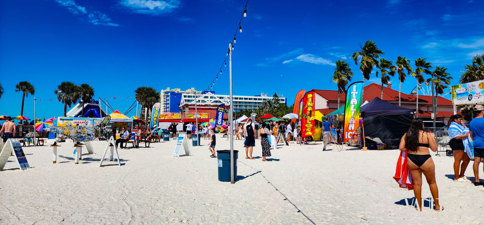Beach scene with people, buildings, and palm trees.