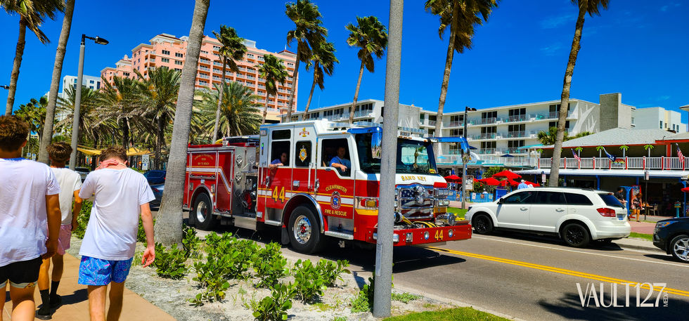 Red fire truck on a sunny street with palm trees.