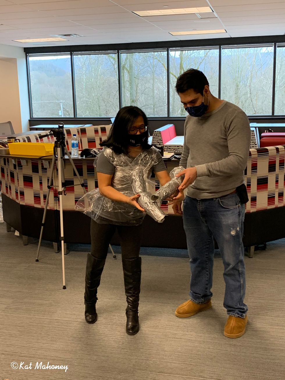 Two people examining an object indoors, wearing masks.