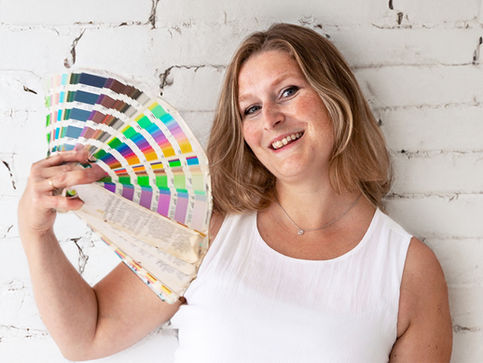 Ashley Fulcher standing in front of a white brick wall, holding a swatch book fanned out like a fan.