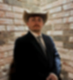 Landry Roberts, wearing a suit and cowboy hat, in front of a brick wall. 