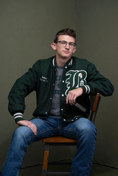 High school senior portrait boy dark green letterman jacket jeans wooden chair Melody Smith Portrait Studio Petersburg VA serving Richmond