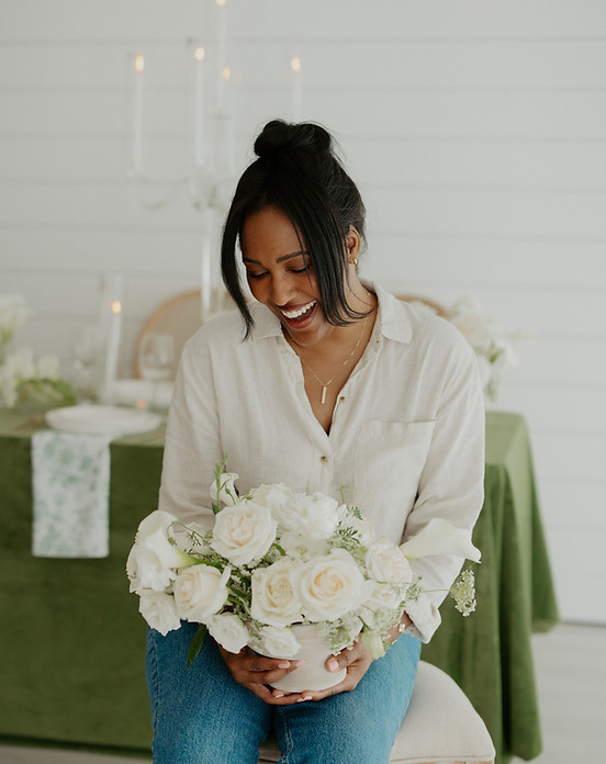 awna smiling, founder of The Scape, with floral arrangements in the background.