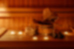 Wooden bucket with spoon, sauna hat, towels and candle light on bench. Traditional finnish