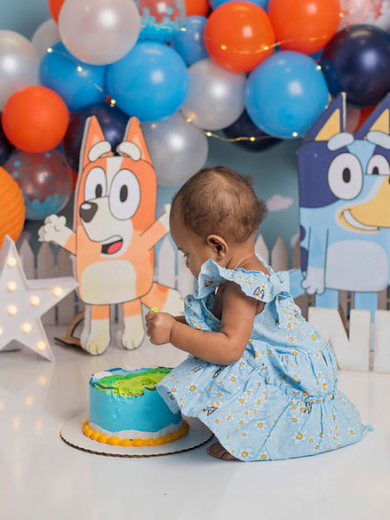Bluey themed cake smash with lots of orange and blue decorations and a little girl eating a bluey themed birthday cake