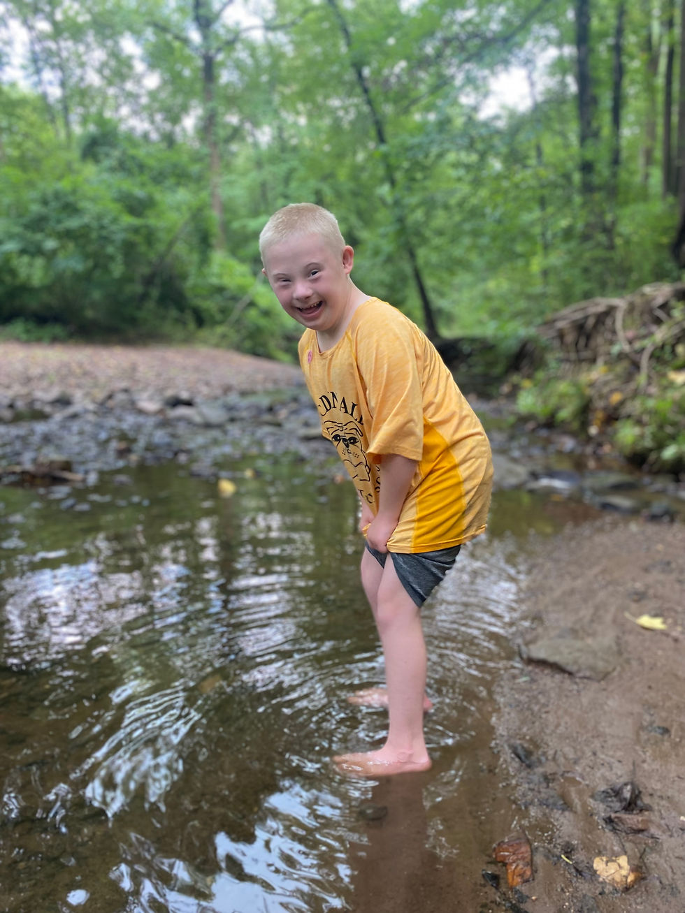 Kathryn's son TJ smiling at the camera while stepping into a creek.