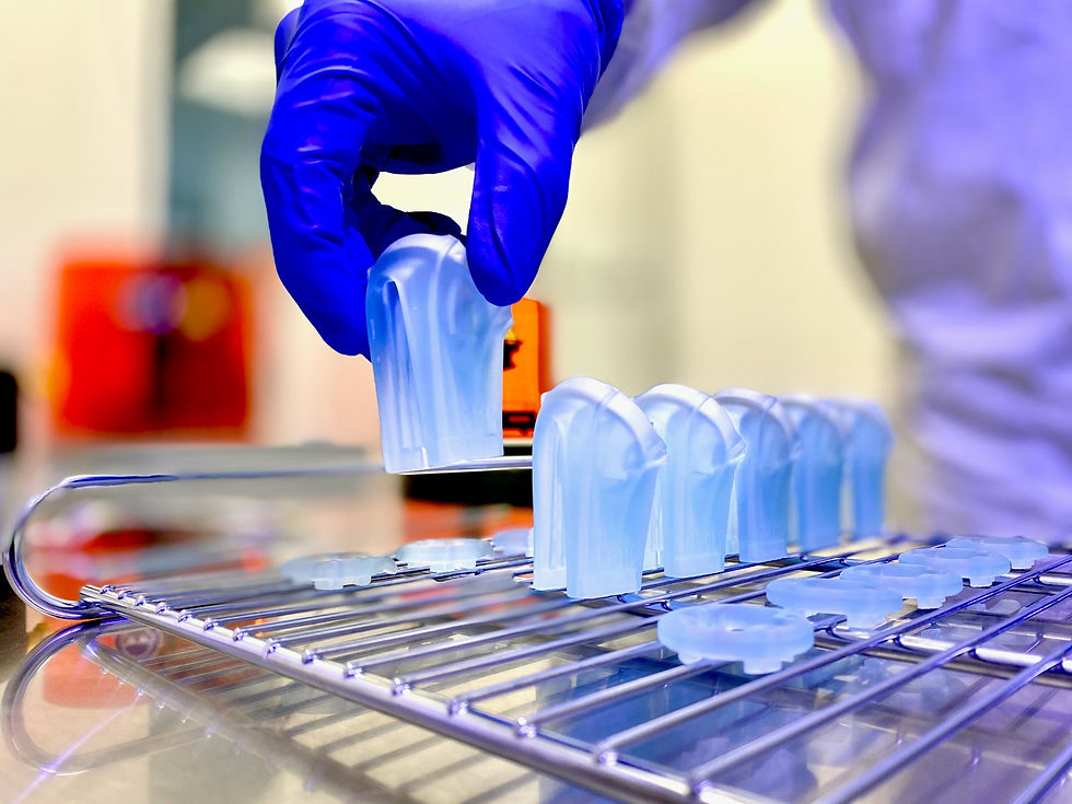 Mehrere blaue 3D-gedruckte Komponenten für die Medizintechnik, eine Hand mit blauem Handschuh hebt eines auf