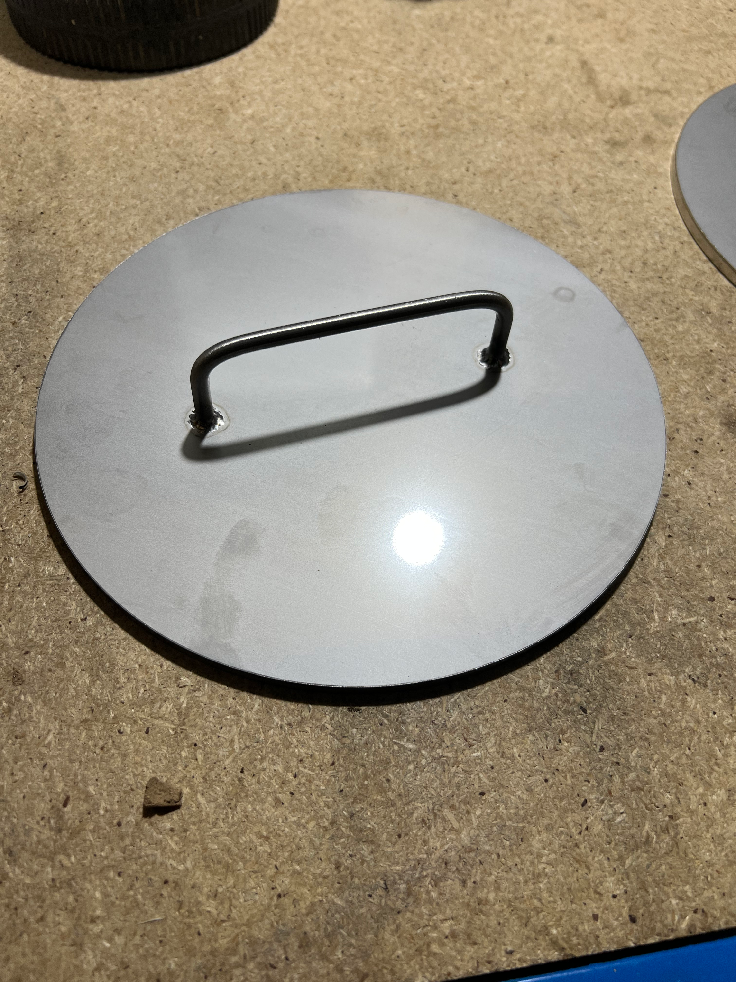 Stainless round disc with stainless handle sitting on a wooden benchtop