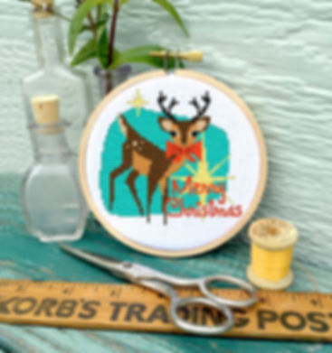 A stitched counted cross stitch pattern of a mid century modern retro Christmas reindeer in turquoise brown and red