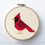 Thumbnail: A retro mid-century modern red cardinal in the style of Charley Harper. It is embroidered in counted cross stitch needlepoint