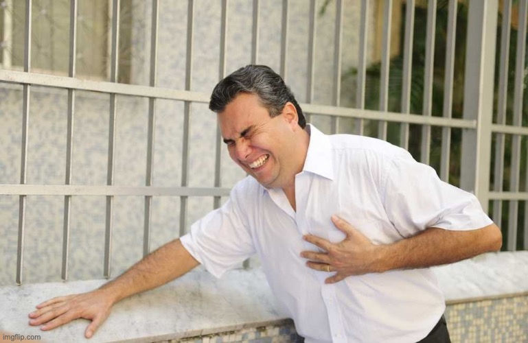 A man in a white shirt clutches his chest in pain, leaning against a tiled wall with a metal fence, displaying distress and discomfort.