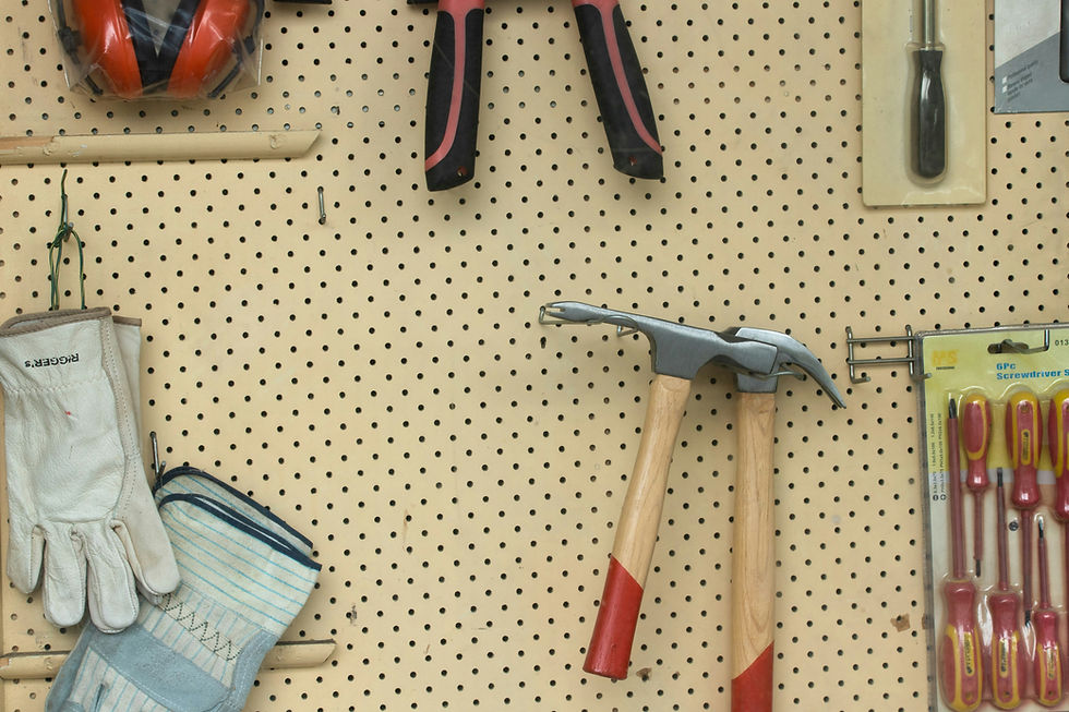Pegboard wall with hanging work gloves, earmuffs, hammers, and packaged screwdrivers in a workshop tool display.