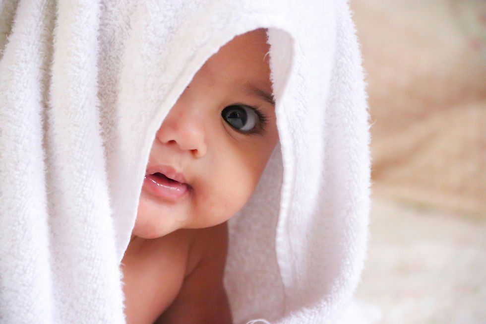 Baby under a white towel, peering out with curious eyes. Soft background, neutral tones, capturing a serene, gentle mood.