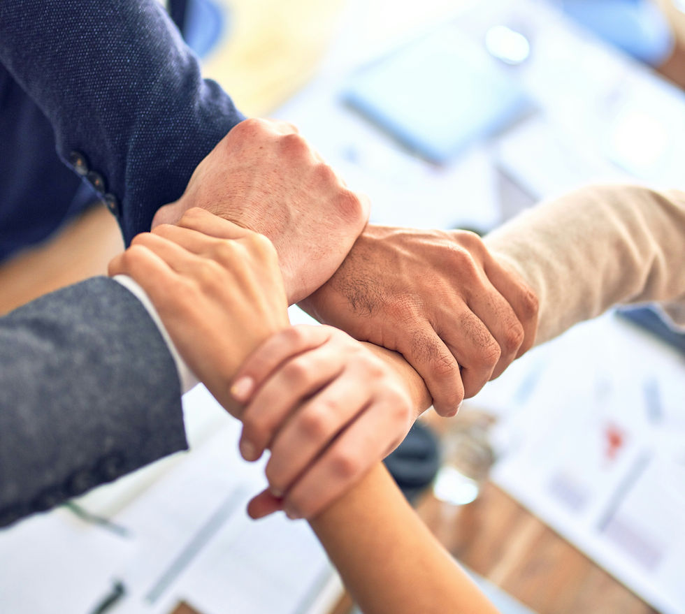 Several diverse hands stacked together in a team huddle, showing unity and support against a bright blurred office background