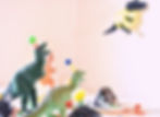Toy dinosaurs wearing party hats surround a table with a slice of cake. Bright colors create a festive atmosphere against a plain backdrop.