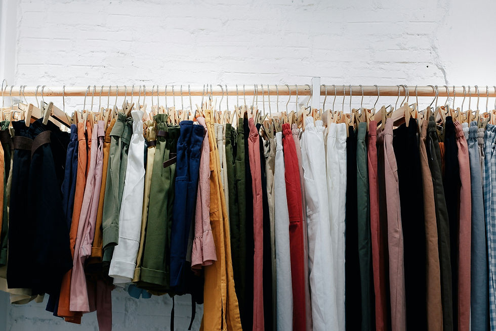 Colorful pants and shorts hang on a rod with wooden hangers against a white brick wall in a neat shop display.