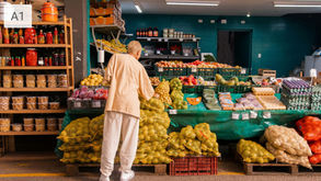A person shops for fruits and vegetables at a market. Shelves hold jars and packaged goods. Green and orange hues dominate the scene.
