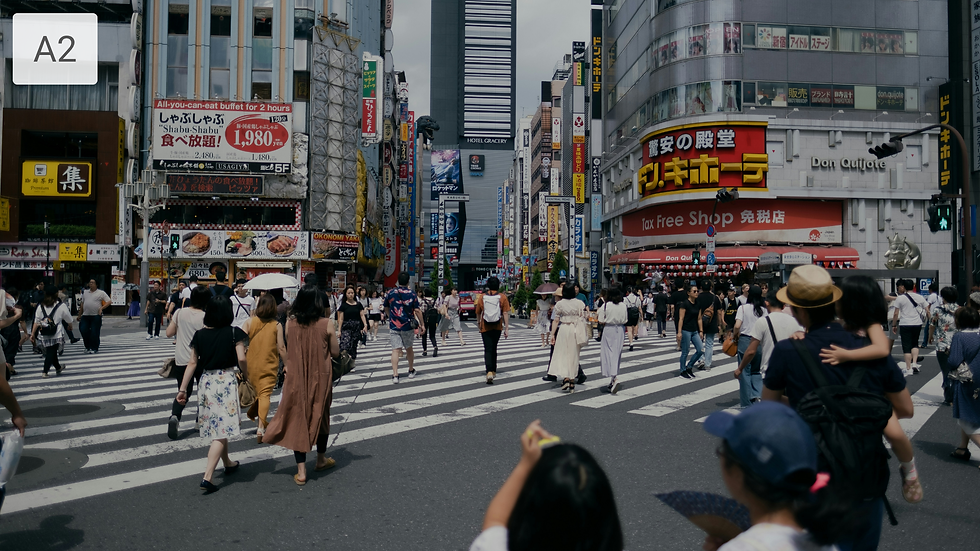 Crowded Tokyo crosswalk with pedestrians, Don Quijote signage, and tall shopfronts lined with Japanese ads under a gray sky.