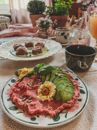 a plate of pink hummus with avocado slices, edible flowers and seeds