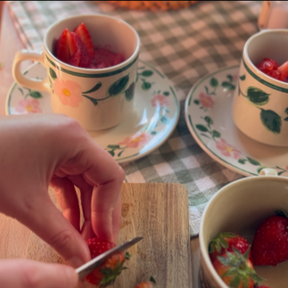a person cutting strawberries to decorate pudding in a teacup