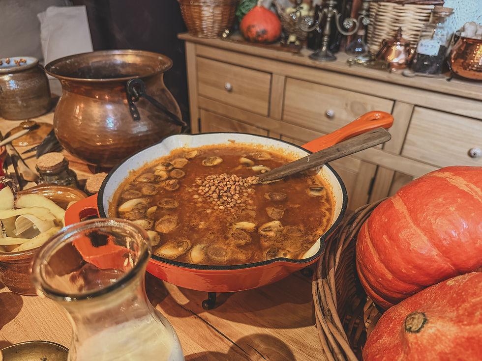 Rustic buffet table with a red Dutch oven of bean-and-mushroom stew, pumpkins, copper pots, and wicker baskets in warm light.