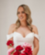 A bride modeling an off-the-shoulder wedding dress with a sweetheart neckline, holding a vibrant bouquet of red roses.