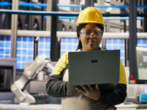 Engineer performing predictive maintenance using laptop, analyzing IoT sensor data, managing operational reliability of photovoltaic systems in smart factory environment